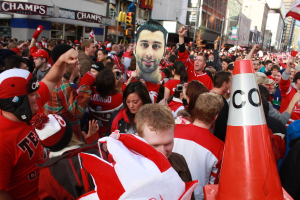 Eine Gruppe von Menschen vor Gebäuden mit einer Ampel und einer Flagge im Hintergrund.