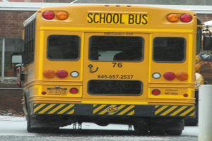 Ein gelber Schulbus steht vor einem Backsteingebäude mit Fenstern.