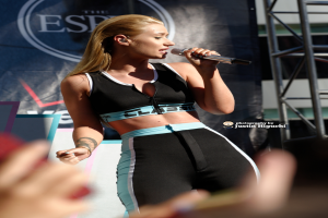 Eine Frau, die in ein Mikrofon singt, mit einem Banner im Hintergrund.