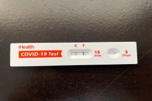 Ein weißer und roter Covid-19-Testthermometer mit Text und Zahlen darauf, das auf einer schwarzen Oberfläche steht.