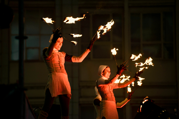 Eine Gruppe von Menschen steht in der Mitte des Bildes, jeder hält eine brennende Fackel, im Hintergrund ein Gebäude.