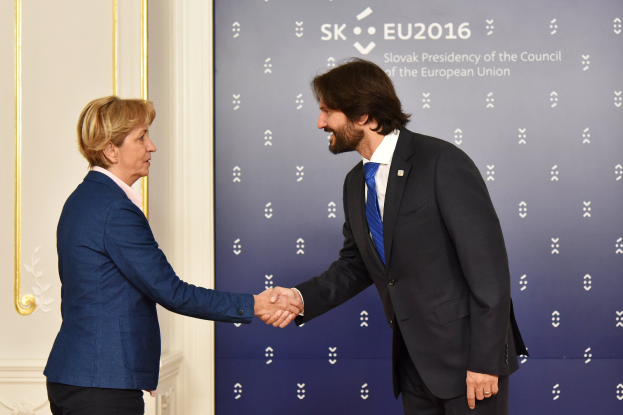Bundeskanzlerin Angela Merkel und Bundeskanzler Joachim Gauck schütteln sich die Hände vor einer Wand mit einem "EU-Gipfel"-Schild und einer Tür im Hintergrund, beide lächeln.