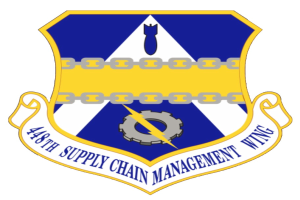 Ein Schild mit einem blauen Hintergrund, ein weißer Stern in der Mitte und ein weißes Banner mit der Aufschrift "Supply Chain Management" in blau, umgeben von einem weißen Rand, mit der schwarzen, fetten Schrift "48th Supply Chain Management Wing"