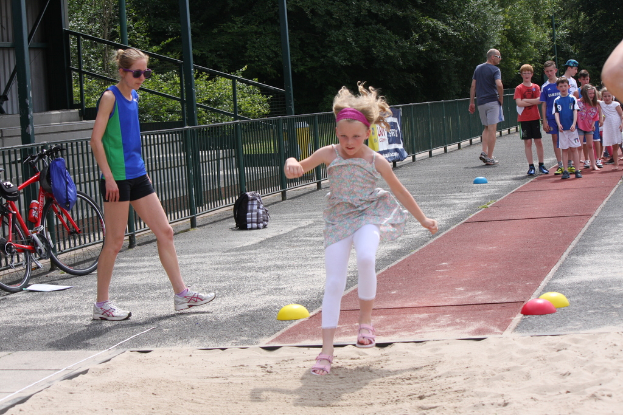 Ein Mödchen steht im Mittelpunkt des Bildes, umgeben von spielenden Menschen, mit einem Fahrrad, einer Begrenzung links, Tälern und Treppen im Hintergrund.