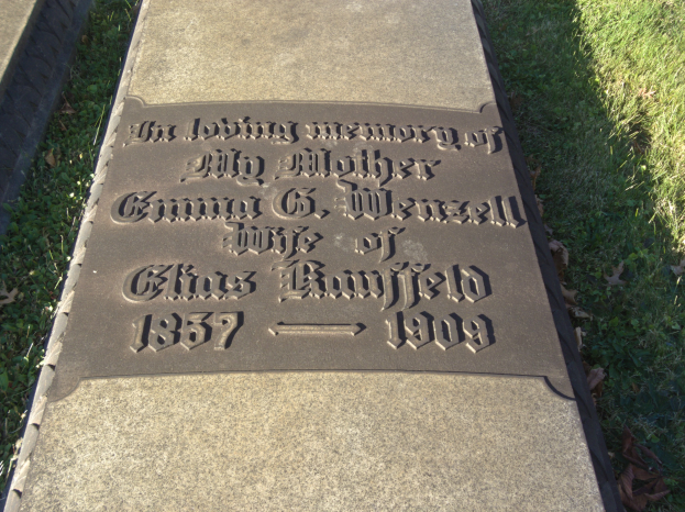 Grabstein mit der Inschrift "In liebevoller Erinnerung an meine Mutter" in einem grasbewachsenen Friedhof mit trockenen Blättern.