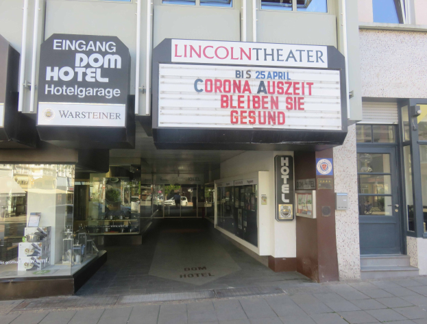 Außenansicht des Lincoln Theaters in Berlin, Deutschland, mit Glasfenstern und -türen sowie einer Schautafel und einem Innenblick, der eine belebte Stadtlandschaft zeigt.