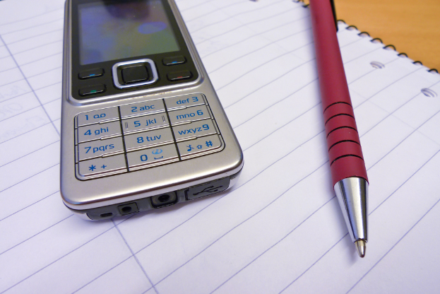 Ein Handy und ein Stift liegen auf einem aufgeschlagenen Buch.