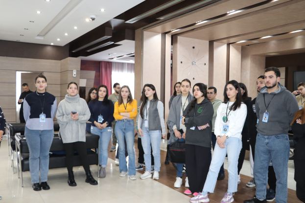 Eine Gruppe von Menschen in einem Raum mit Stühlen, Sofas, Vorhängen und Deckenleuchten, einige tragen ID-Karten und nehmen an einer Schulung an der Universität Ankara teil.