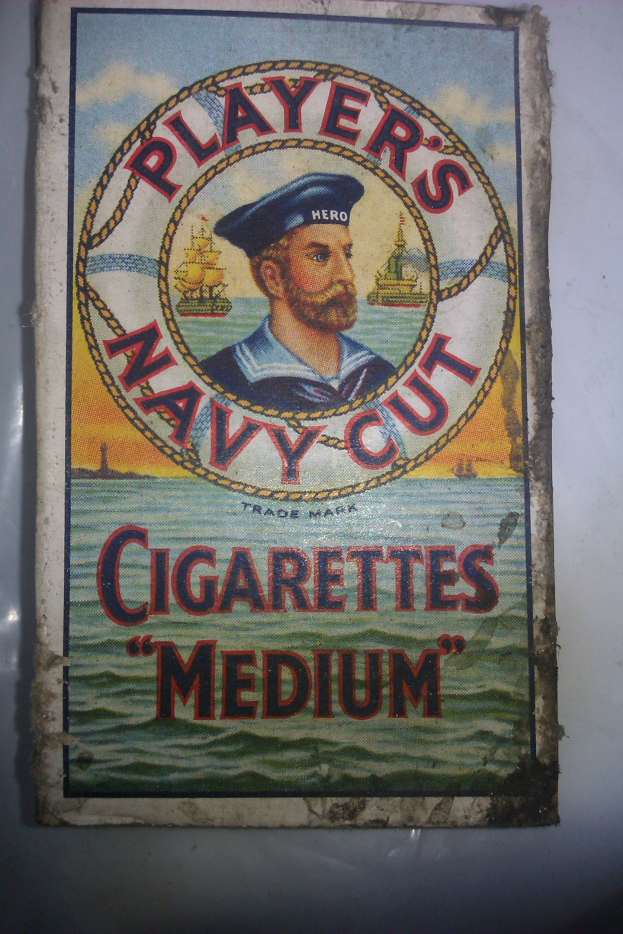 Plakat, das "Player's Navy Cut Cigarettes Medium" bewirbt, zeigt eine Person in einer marineblauen Uniform mit weißem Hemd und roter Krawatte, die Arme verschränkt und einen strengen Gesichtsausdruck hat, Text in fetter schwarzer Schrift mit weißem Rand.
