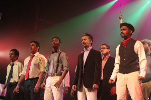 Eine Gruppe von Männern steht auf einer Bühne und spielt ein Drama mit grünen Spotlights im Hintergrund.