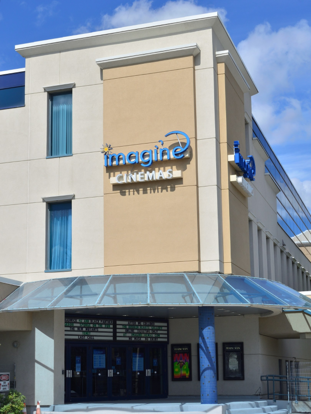 Außenansicht des Imagine Cinemas in San Diego, Kalifornien, mit einem Gebäude mit Fenstern, Türen, einem Schild, Pflanzen, Polen, einer Treppe und einem bewölkten Himmel.