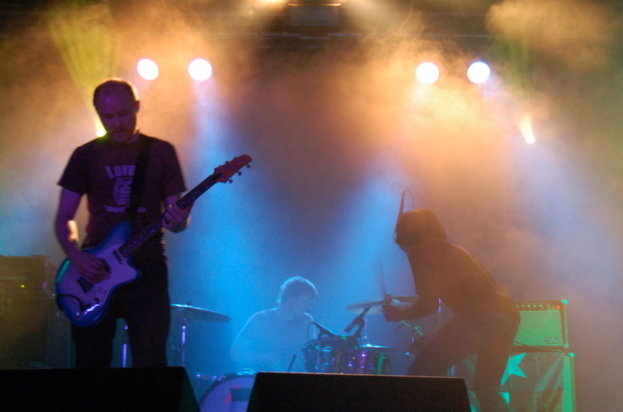 Ein musikalisches Konzert mit Lichtern oben, Musikern in der Mitte und Lautsprechern auf beiden Seiten.