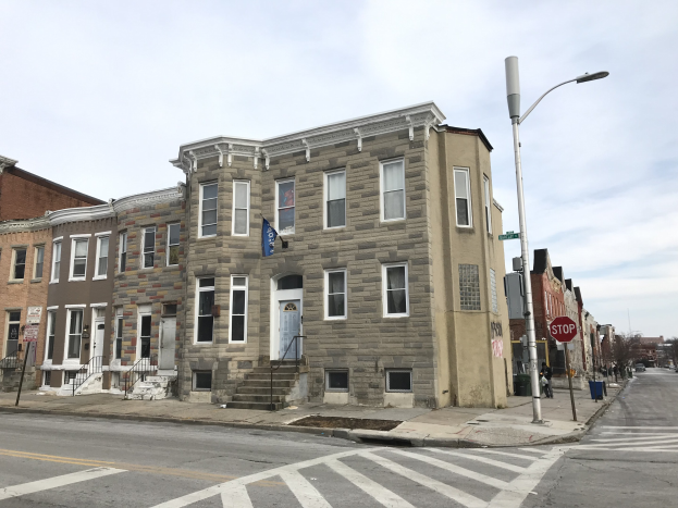 Eine Reihe moderner Häuser mit Fenstern, Türen, Geländern, Straßenlaternen und Schildern an einer Ecke in einem Wohnprojekt in Philadelphia, mit Fahrzeugen auf der Straße, Bäumen und einem bewölkten Himmel im Hintergrund.