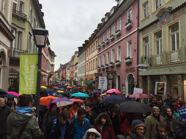 Eine große Gruppe von Menschen geht mit Schirmen die Straße entlang, einige tragen Taschen und halten Schilder, während sie an einem climate strike in Deutschland teilnehmen.