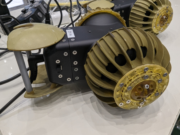 Nahaufnahme eines schlanken, metallischen 3D-gedruckten Robotikbauteils auf einem Tisch umgeben von Kabeln.