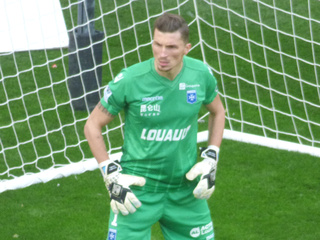 Ein Torwart in grüner Uniform steht vor einem Fußballtor auf saftigem Grün, Handschuhe tragend.