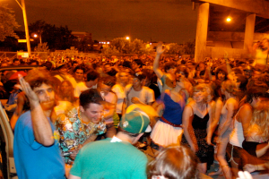 Menschen tanzen im Vordergrund eines Konzerts mit Lichtern, Pfählen, Bäumen und anderen Gegenständen im Hintergrund.