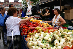 Eine Gruppe von Menschen, die sich draußen in der Nähe von Gebäuden und Bäumen aufhalten, mit Gemüse in Plastikbehältern und einer Pappkiste in der Nähe.