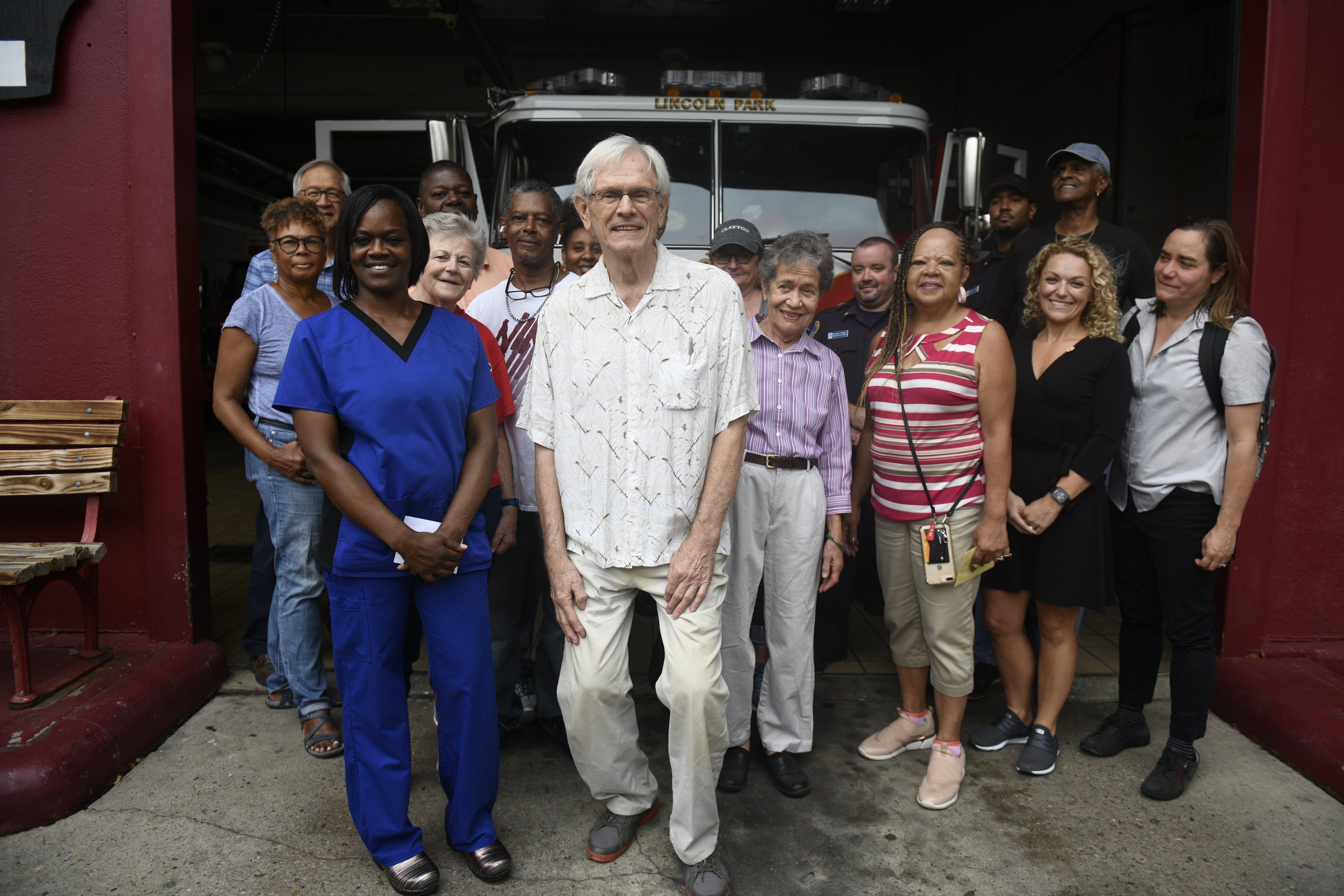 Gruppe von Freiwilligen vor einem Feuerwehrauto, mit einer Bank auf der linken Seite und einer Wand im Hintergrund.