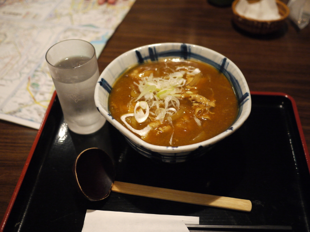 Ein Tablett mit einem Glas, Löffel, einem umschlagähnlichen Objekt, einer Suppenschüssel und einer Karte oben links, mit einem Korb und einigen Gegenständen oben rechts.