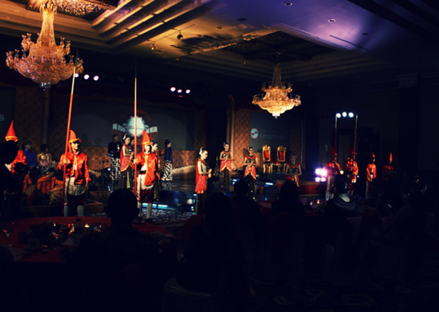 Eine Gruppe von Menschen sitzt und schaut eine Show mit zwei Kronleuchtern an der Decke.