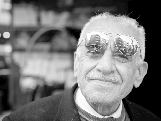 Ein Mann mit einem lachenden Gesicht, der eine Schutzbrille trägt, vor einem unscharfen Hintergrund in einem Schwarz-Weiß-Bild.