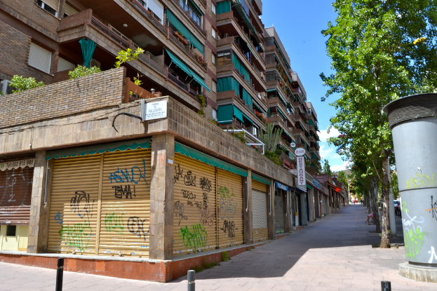 Eine Szene mit Gebäuden mit Fenstern, grünen Kleidungsstücken, Geschäften, Schildern und umgebenden Bäumen und Pflanzen.