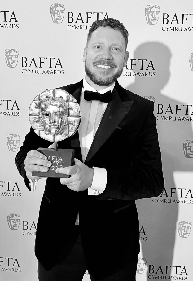 Ein Mann in einem Smoking, der eine BAFTA-Auszeichnung hält und lächelt, mit einer 'BAFTA Awards 2018'-Rückwand.