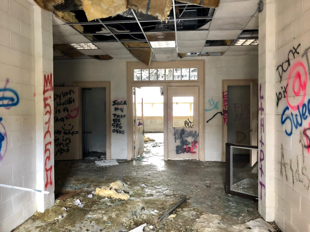 Verlassenes Gebäude mit Graffiti-beschmierten Wänden und Decke, Schutt auf dem Boden, mehrere Türen und Fenster im Hintergrund und verstreute Gegenstände.