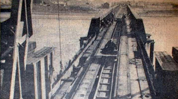 Ein Schwarz-Weiß-Foto einer Bahngleise mit einer Brücke im Hintergrund, umgeben von Werkzeugen und Materialien.