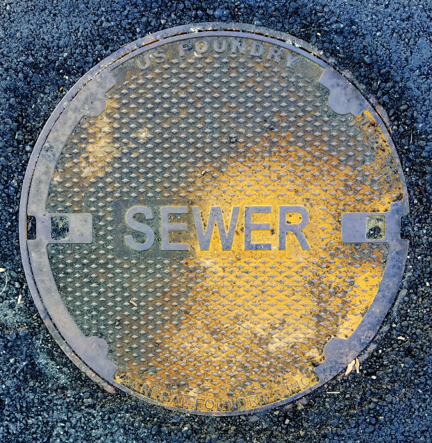 Ein metallener Gullydeckel auf der Straße mit der Aufschrift "Sewer"