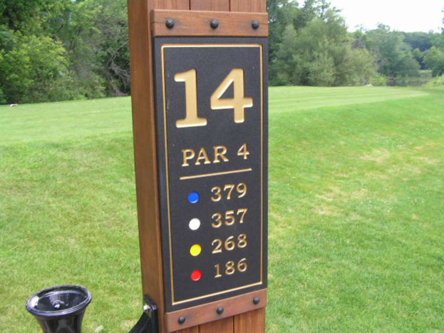 Ein hölzerner Pfahl mit Zahlen darauf steht vor einem grünen Bereich mit Bäumen.