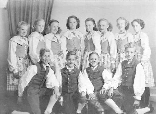 Schwarz-weiß-Foto von Kindern, die vor einer Vorhangwand mit dem Text "1930er Kinder-Schule" unten posieren