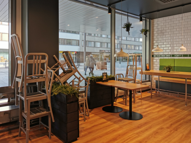 Ein Restaurant-Innenraum mit Holztischen und -stühlen, betrachtet durch ein großes Fenster, das eine Straßenszene in Berlin, Deutschland, zeigt.