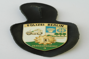 Ein Polizeistern mit der Aufschrift "Polizei Berlin" auf einem blauen Schild mit einem weißen Stern in der Mitte, umgeben von einem weißen Rand.