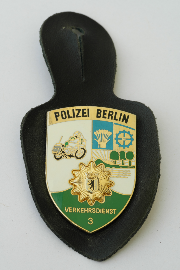 Ein Polizeistern mit der Aufschrift "Polizei Berlin" auf einem blauen Schild mit einem weißen Stern in der Mitte, umgeben von einem weißen Rand.
