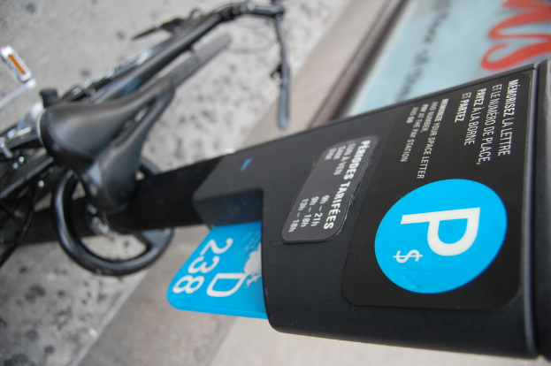 Ein Fahrrad ist auf dem Boden neben einem Parkscheinautomaten geparkt, wobei ein Gehweg unten im Bild sichtbar ist.