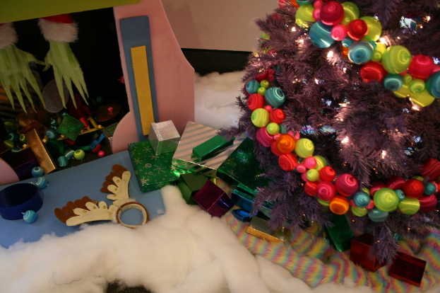 Drinnen: Ein geschmückter Weihnachtsbaum rechts, Geschenkboxen und Dekorationen in der Mitte, eine Hütte mit Dekorationen oben links und Baumwolle und Wolle unten.