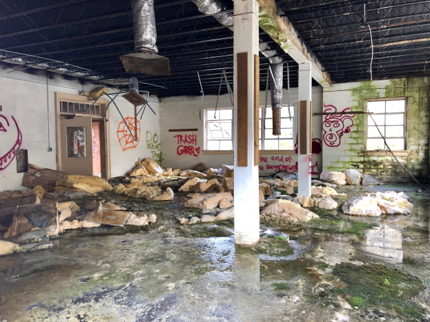 Ein verlassenes Gebäude mit Graffiti an den Wänden, Säulen und Fenstern, das eine Tür, ein Dach mit Metallstangen und Deckenlampen sowie überflutete Böden zeigt und die Zerstörung durch Hurrikan Sandy demonstriert.