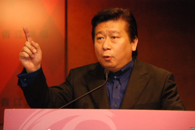 Ein Mann im Anzug und mit Krawatte hält eine Rede an einem Rednerpult mit einem Mikrofon und sieht ernst und professionell aus.