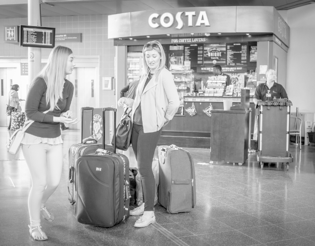 Zwei Frauen vor Gep├Ąckst├╝cken mit einem Kaffeeschop im Hintergrund, wahrscheinlich am Flughafen.