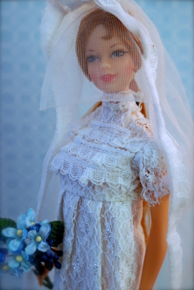 Eine Puppe in einem Kleid, Schleier und mit einem Blumenstrauß, vor einem unscharfen Hintergrund.