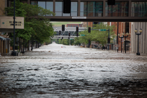 Eine überflutete Stadtstraße mit Wasser auf der Straße, Polen, Laternen, Schildern, Verkehrsampeln, Bäumen, Gebäuden und einer Brücke im Hintergrund.