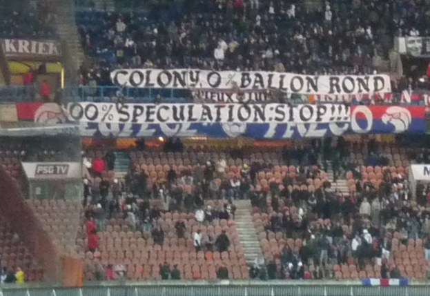 Ein Stadion voller Menschen, Schilder und Stühle, mit einem Zaun unten und einer Treppe links.