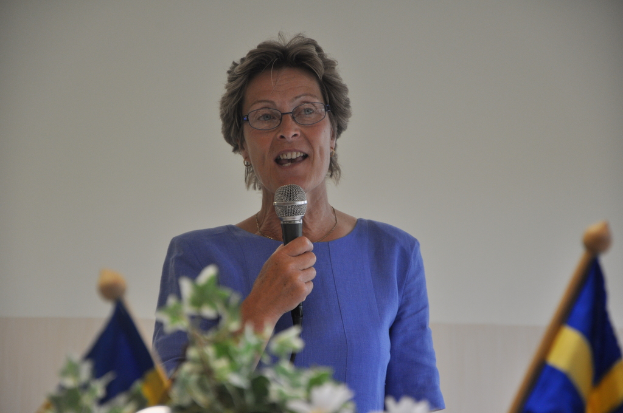 Eine Frau steht an einem Podium mit zwei Flaggen und spricht in ein Mikrofon.