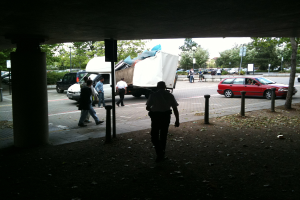 Eine belebte Straßenszene mit zahlreichen Fußgängern, einem Auto und einem Lastwagen.