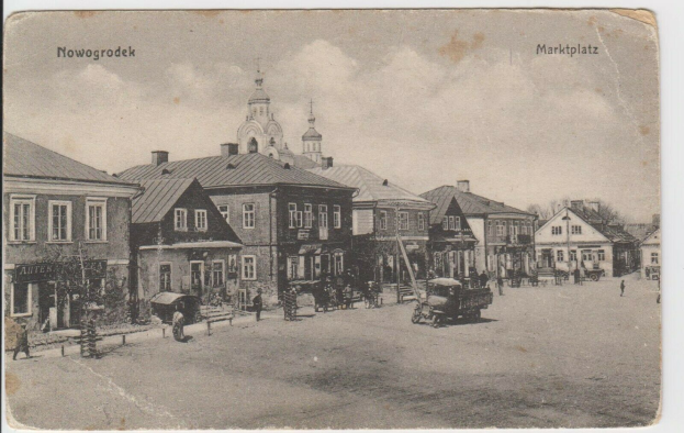 Ein Schwarz-Weiß-Foto einer Straße in Nowogrodeek, Deutschland, mit Gebäuden, Menschen, Wagen, Pfölen und Bäumen sowie dem Text "Marktplatz in Nowogrodeek, Deutschland" oben und unten.