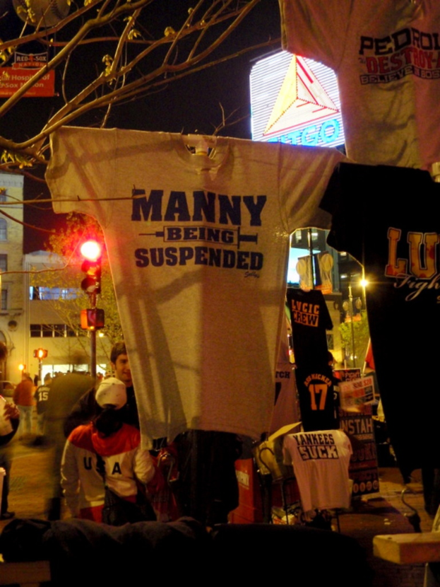 Eine Gruppe von Menschen in T-Shirts, mit Ampeln, Bäumen, Pfählen und Gebäuden im Hintergrund.