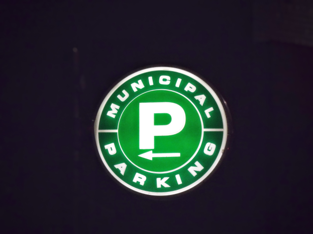 Ein grünes Parkhausschild an der Seite eines Gebäudes mit der Aufschrift "Städtisches Parkhaus" in Weiß gegen einen schwarzen Hintergrund.