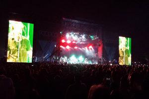 Ein Konzertbild mit einer Menge unten, einem Bildschirm links und einem weiteren rechts.